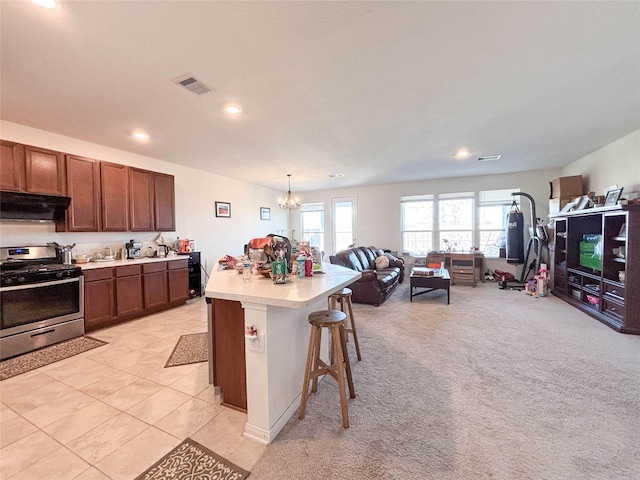 kitchen featuring an island with sink, a kitchen breakfast bar, hanging light fixtures, stainless steel gas range oven, and an inviting chandelier