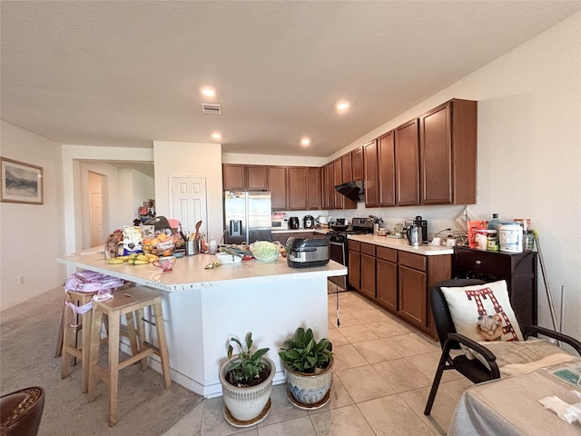 kitchen featuring a kitchen bar, light tile patterned floors, stainless steel appliances, and a center island with sink