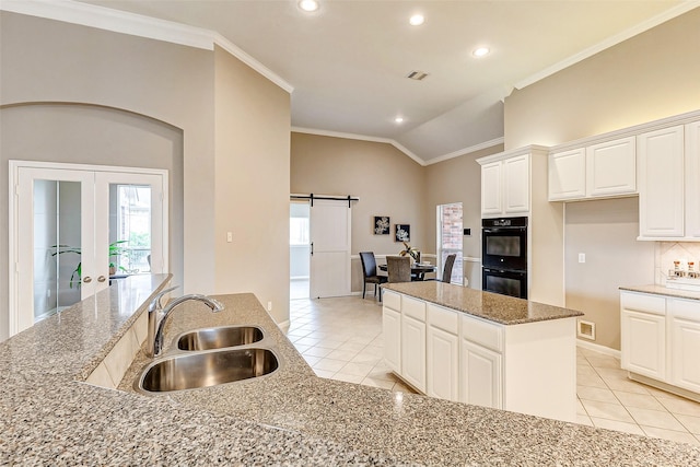 kitchen with sink, double oven, a center island, light stone counters, and a barn door