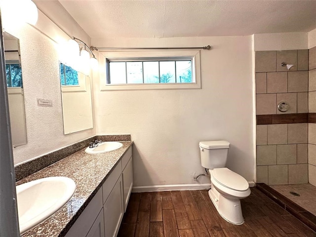 bathroom with tiled shower, toilet, a textured ceiling, vanity, and hardwood / wood-style floors