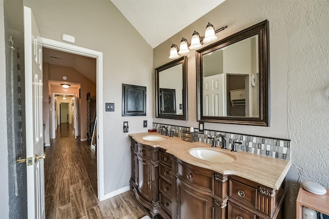 full bath with lofted ceiling, double vanity, wood finished floors, and a sink