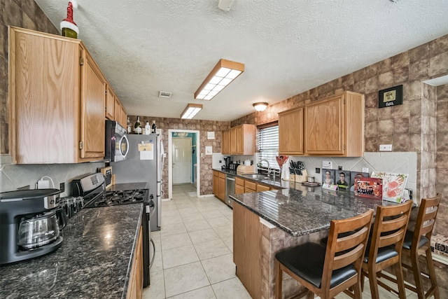 kitchen featuring light tile patterned floors, stainless steel appliances, a peninsula, a sink, and decorative backsplash