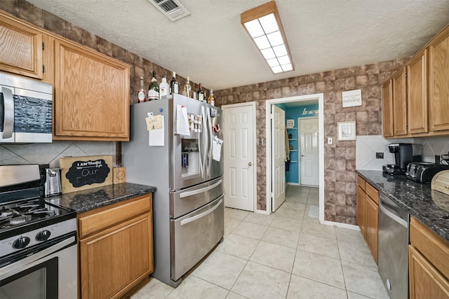 kitchen with a textured ceiling, light tile patterned floors, stainless steel appliances, visible vents, and dark stone counters