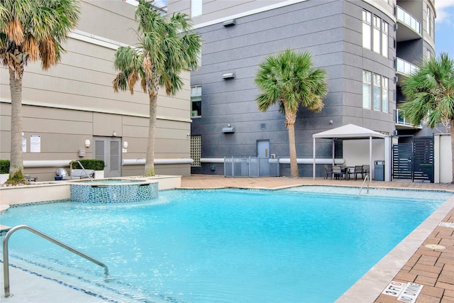 view of pool with cooling unit, pool water feature, and a hot tub