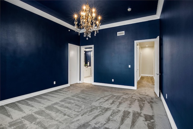 spare room with a chandelier, carpet, baseboards, visible vents, and ornamental molding