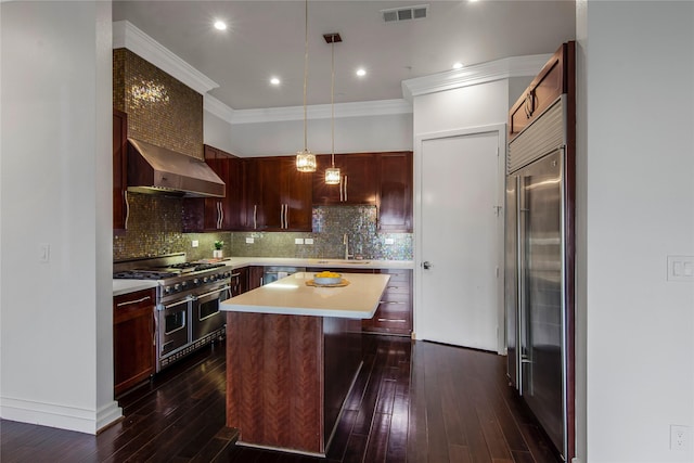 kitchen featuring visible vents, high end appliances, light countertops, wall chimney exhaust hood, and dark wood finished floors
