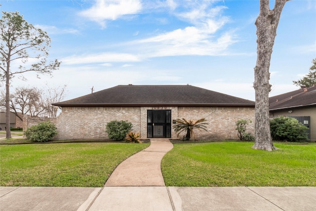 view of front of property featuring a front yard, brick siding, and roof with shingles