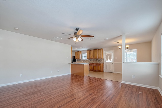 unfurnished living room with ceiling fan with notable chandelier, a wealth of natural light, and light hardwood / wood-style flooring