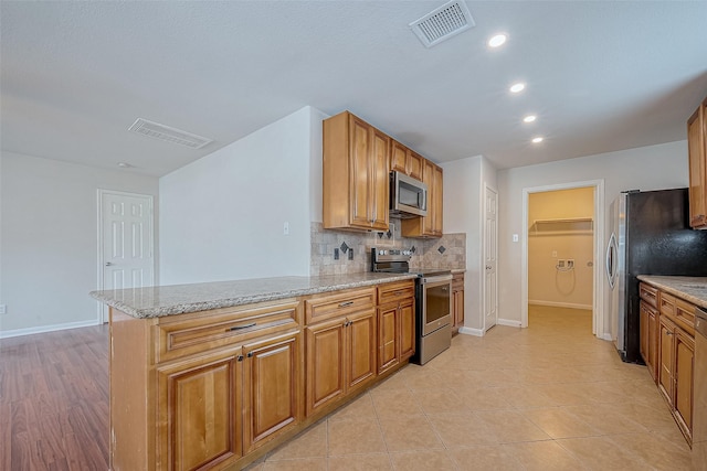 kitchen with light stone counters, light tile patterned floors, appliances with stainless steel finishes, kitchen peninsula, and backsplash