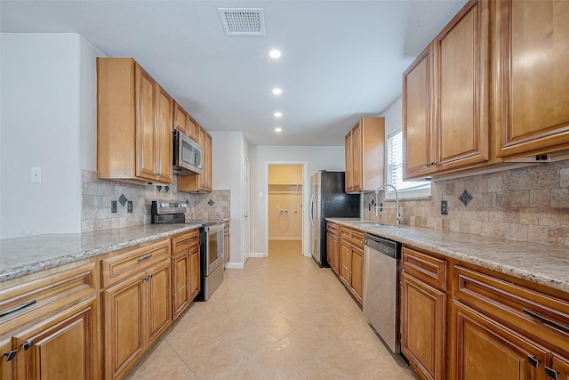 kitchen featuring light stone countertops, appliances with stainless steel finishes, sink, and light tile patterned flooring