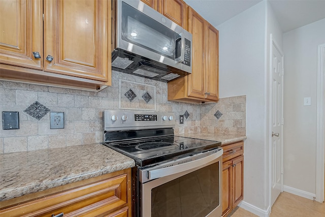 kitchen featuring stainless steel appliances, tasteful backsplash, light stone countertops, and light tile patterned floors