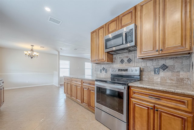 kitchen with appliances with stainless steel finishes, light tile patterned floors, backsplash, and light stone counters