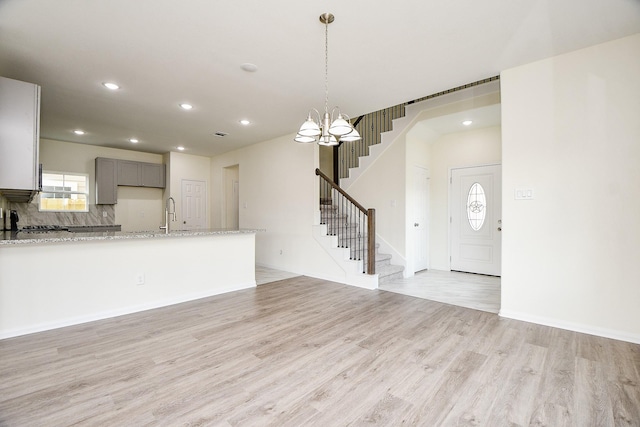 unfurnished living room with an inviting chandelier, sink, and light hardwood / wood-style flooring