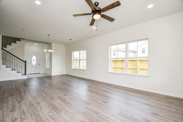 unfurnished living room with ceiling fan with notable chandelier and light hardwood / wood-style flooring