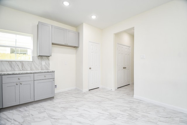 kitchen featuring gray cabinets, light stone countertops, and backsplash