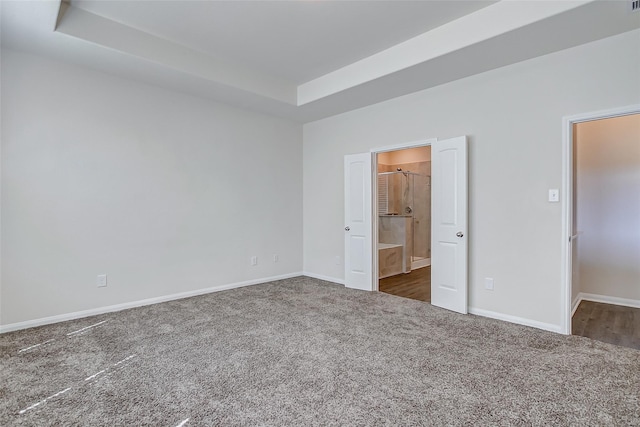 unfurnished bedroom with ensuite bath, a raised ceiling, and dark carpet