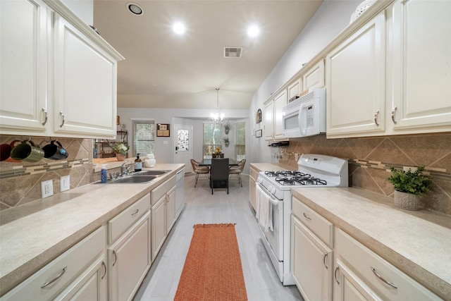 kitchen featuring sink, vaulted ceiling, a notable chandelier, pendant lighting, and white appliances