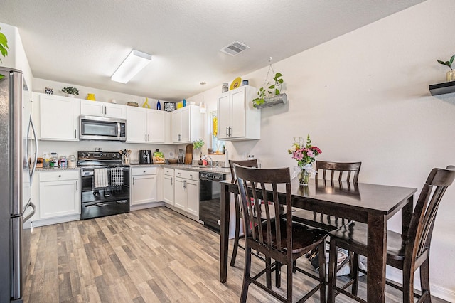 kitchen featuring white cabinetry, black appliances, a textured ceiling, and light wood-type flooring