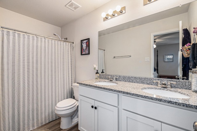 bathroom with wood-type flooring, vanity, ceiling fan, walk in shower, and toilet