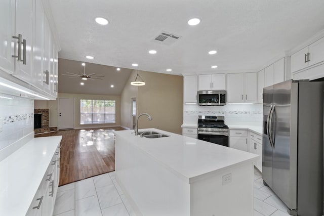 kitchen with sink, a kitchen island with sink, stainless steel appliances, white cabinets, and decorative backsplash