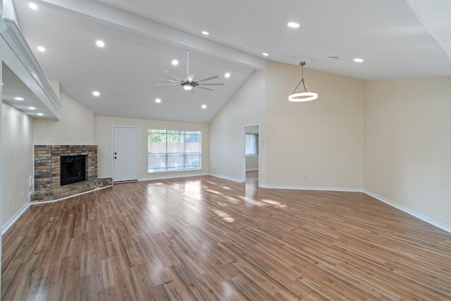 unfurnished living room featuring beamed ceiling, ceiling fan, a fireplace, and light hardwood / wood-style flooring