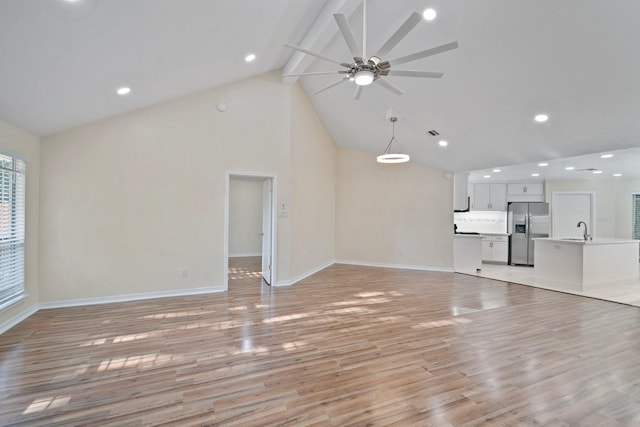 unfurnished living room with sink, high vaulted ceiling, light wood-type flooring, beamed ceiling, and ceiling fan