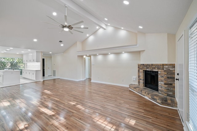 unfurnished living room featuring high vaulted ceiling, ceiling fan, a brick fireplace, beam ceiling, and light hardwood / wood-style flooring