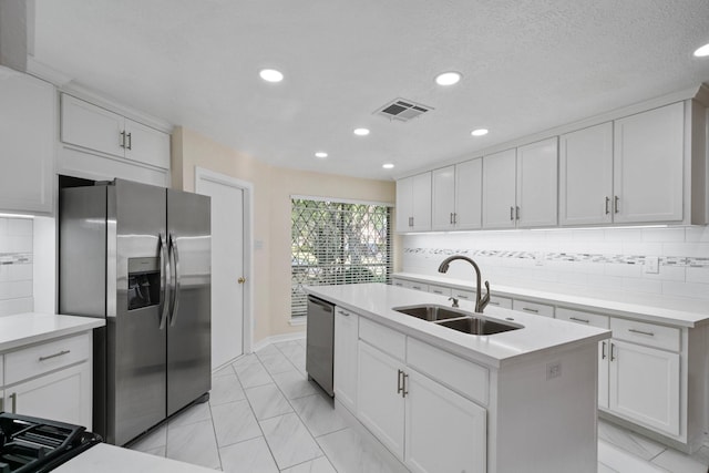 kitchen featuring sink, appliances with stainless steel finishes, white cabinetry, tasteful backsplash, and an island with sink