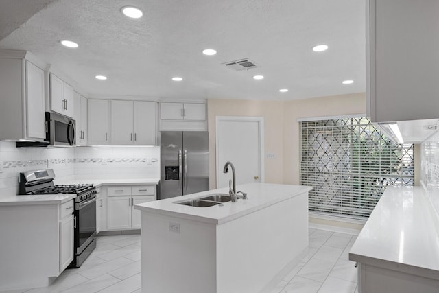 kitchen with sink, appliances with stainless steel finishes, white cabinets, a center island with sink, and decorative backsplash