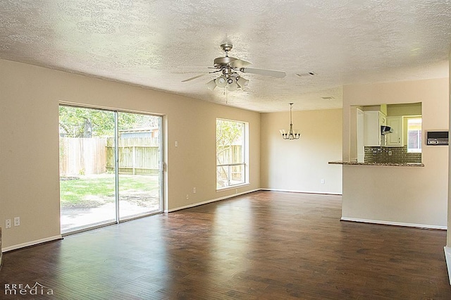 unfurnished living room featuring dark wood-type flooring, ceiling fan with notable chandelier, a textured ceiling, and a wealth of natural light