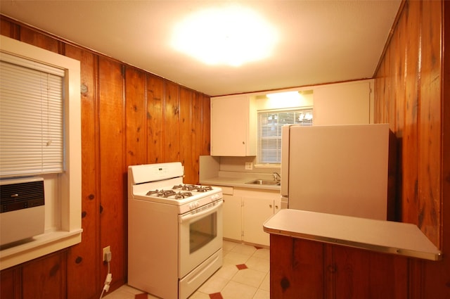 kitchen with white appliances, wooden walls, sink, and white cabinets