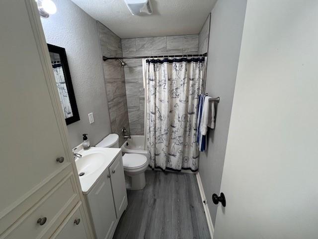 full bathroom with shower / tub combo, vanity, wood-type flooring, a textured ceiling, and toilet