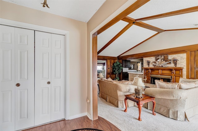 living room featuring vaulted ceiling with beams, hardwood / wood-style flooring, a textured ceiling, and a brick fireplace