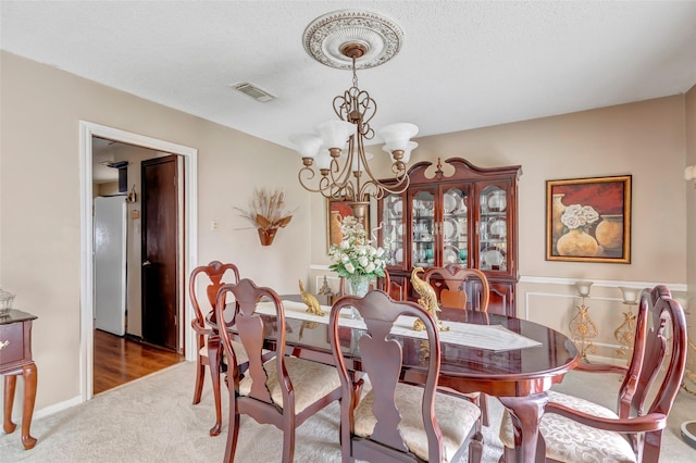 carpeted dining area with an inviting chandelier and a textured ceiling