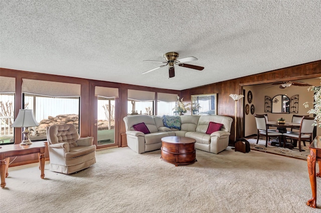 carpeted living room featuring wooden walls, a textured ceiling, and ceiling fan