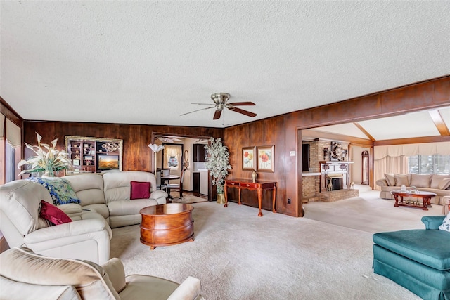 carpeted living room with ceiling fan, wooden walls, a brick fireplace, and a textured ceiling