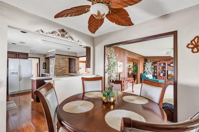 dining room with crown molding, dark wood-type flooring, ceiling fan, and a textured ceiling