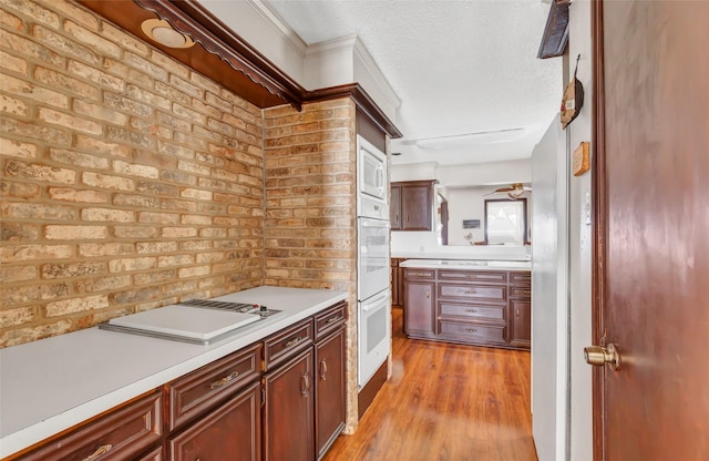 kitchen with white appliances, brick wall, a textured ceiling, and light wood-type flooring