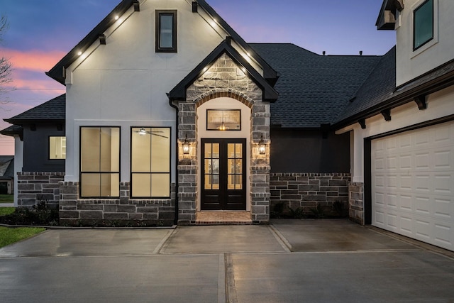 exterior entry at dusk featuring a garage and french doors