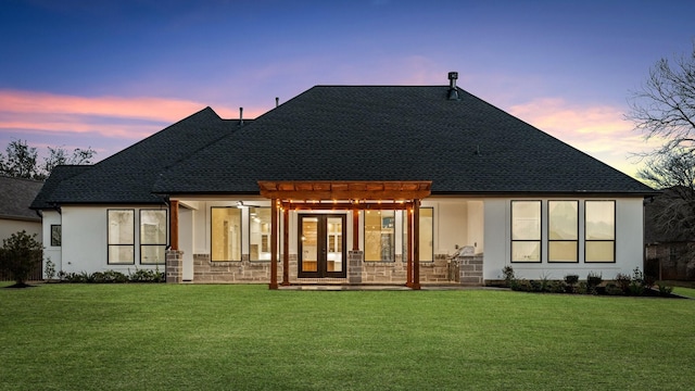 back house at dusk featuring french doors, a lawn, and a pergola