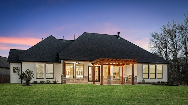 back house at dusk featuring a lawn and a pergola