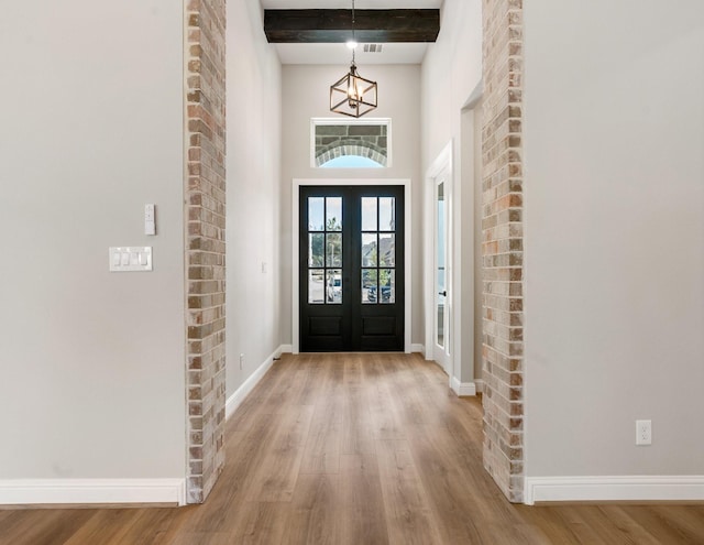 foyer with beam ceiling, an inviting chandelier, light wood-type flooring, and french doors