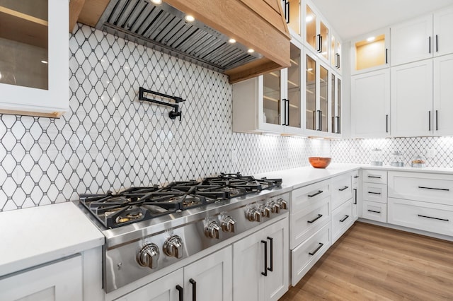 kitchen featuring stainless steel gas cooktop, white cabinetry, tasteful backsplash, custom range hood, and light hardwood / wood-style floors