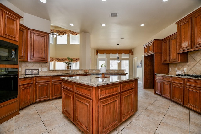 kitchen featuring light tile patterned floors, decorative light fixtures, black appliances, and a kitchen island