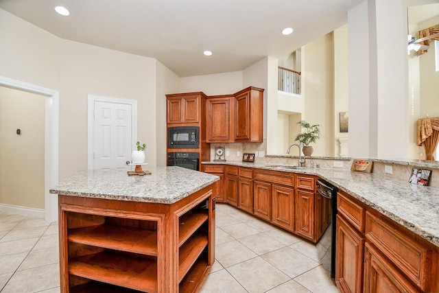 kitchen with sink, a center island, light tile patterned floors, light stone counters, and black appliances