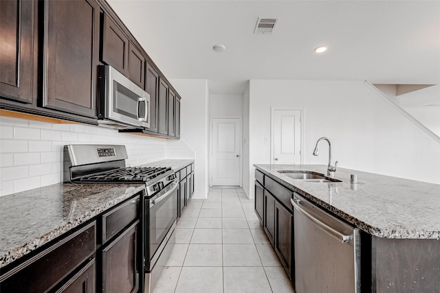 kitchen featuring light tile patterned flooring, appliances with stainless steel finishes, sink, backsplash, and a center island with sink