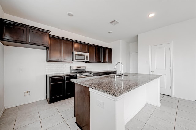 kitchen with sink, light stone counters, stainless steel appliances, a kitchen island with sink, and backsplash