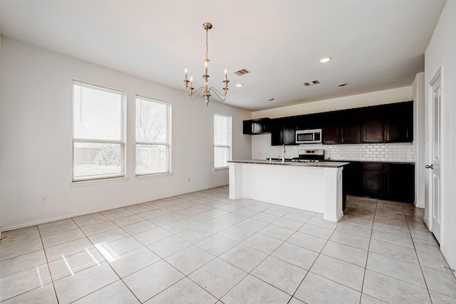 kitchen featuring tasteful backsplash, hanging light fixtures, a center island with sink, appliances with stainless steel finishes, and a notable chandelier