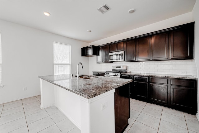 kitchen with sink, appliances with stainless steel finishes, backsplash, light stone counters, and a center island with sink