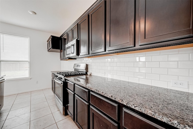 kitchen with appliances with stainless steel finishes, tasteful backsplash, light tile patterned floors, dark brown cabinetry, and light stone counters